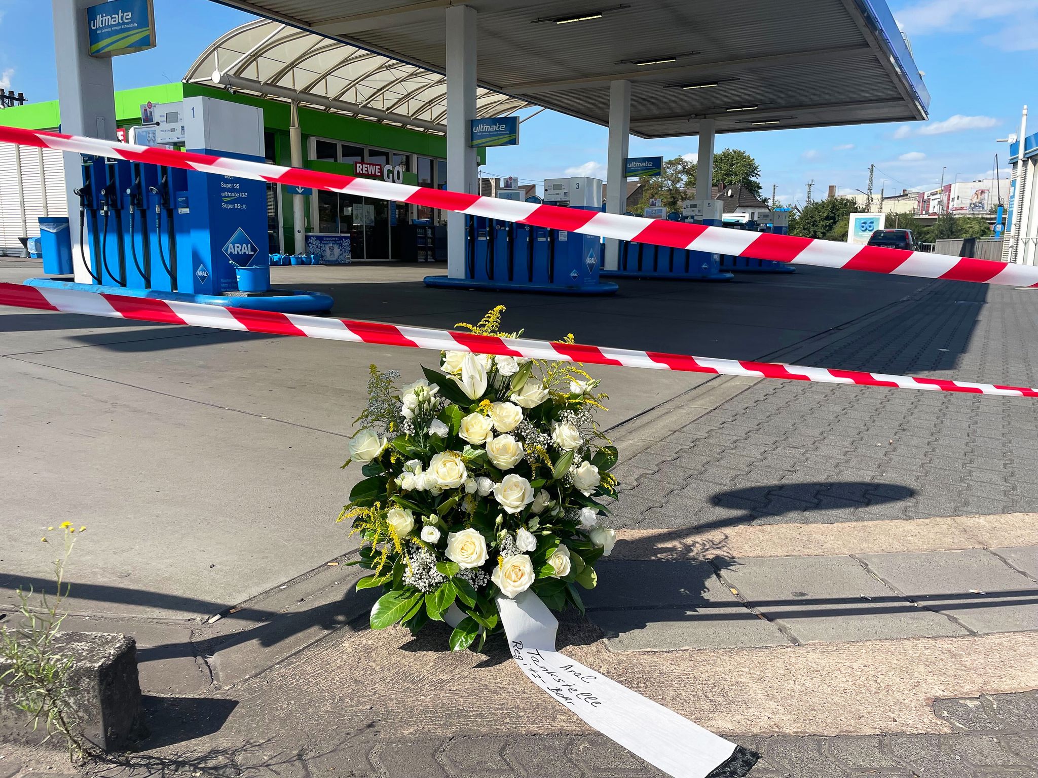Ein großer Blumenkranz steht vor der überfallenen Tankstelle.
