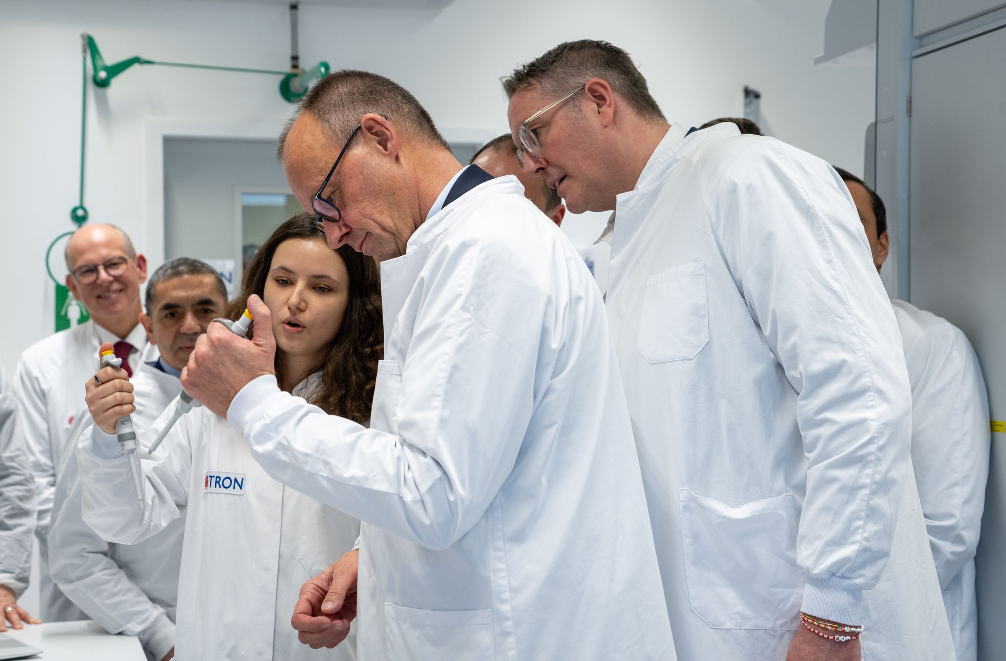 Nein, pipettiert habe er noch nie, sagt Kanzler Merz (Mitte) und bekommt es von einer Doktorandin erklärt. 